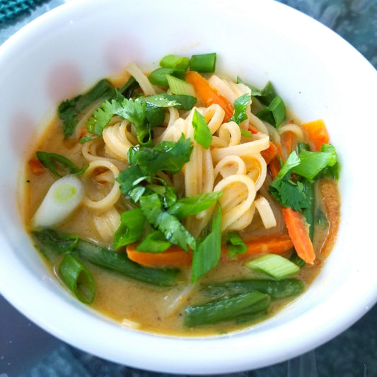 Bowl filled with boodles, green beans, carrots, with small pieces of green onions and cilantro on top