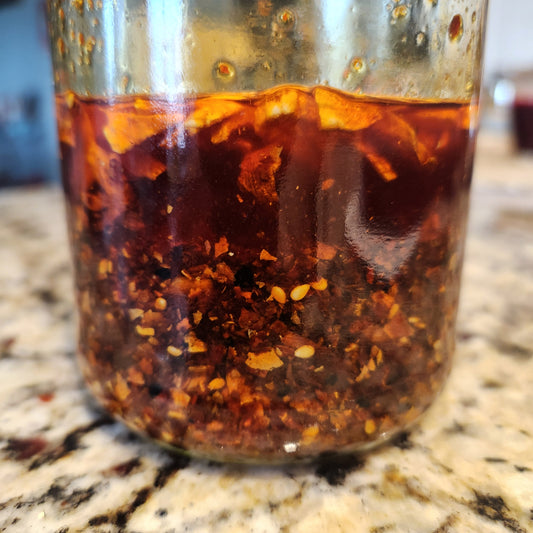 Glass jar filled with red oil and pieces of chiles, shallots and garlic