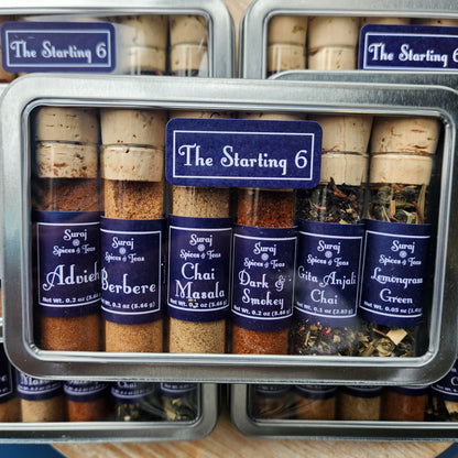 6 cork topped glass bottles filled with various blends in a metal window rectangular tin.