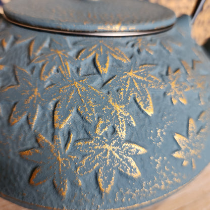 Close up of golden maple leaf pattern on turquoise teapot